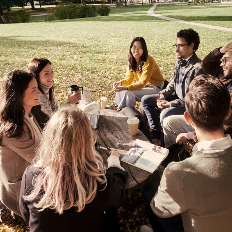Happy students sitting around a table outdoors on campus.